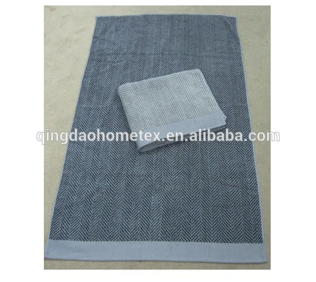 Navy herringbone towels with light grey borders, one folded on top of the other on a concrete floor