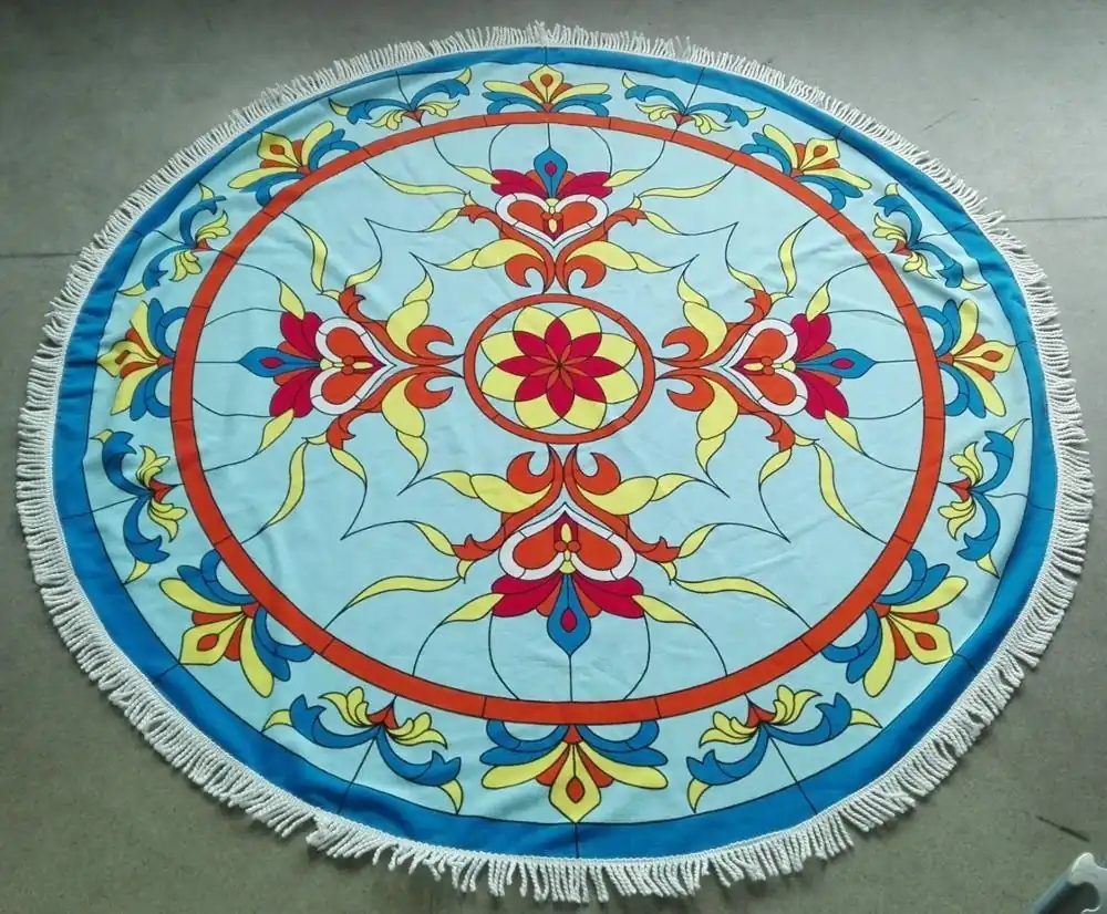 Round blue beach towel with colorful floral mandala print and white fringe, laid flat on a concrete floor