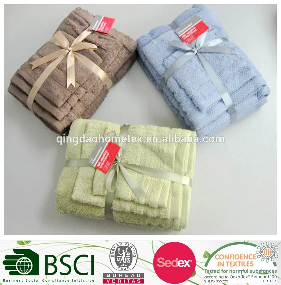 Three stacked towel sets in brown, blue, and green tied with ribbon bows on a white surface