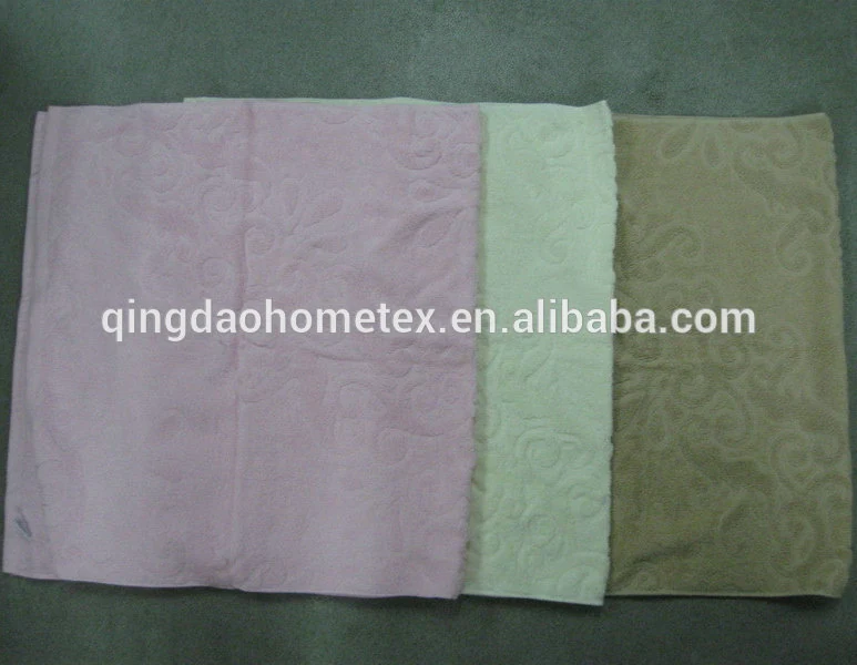 Three folded jacquard towels in pink, mint green, and tan laid side by side on a gray surface