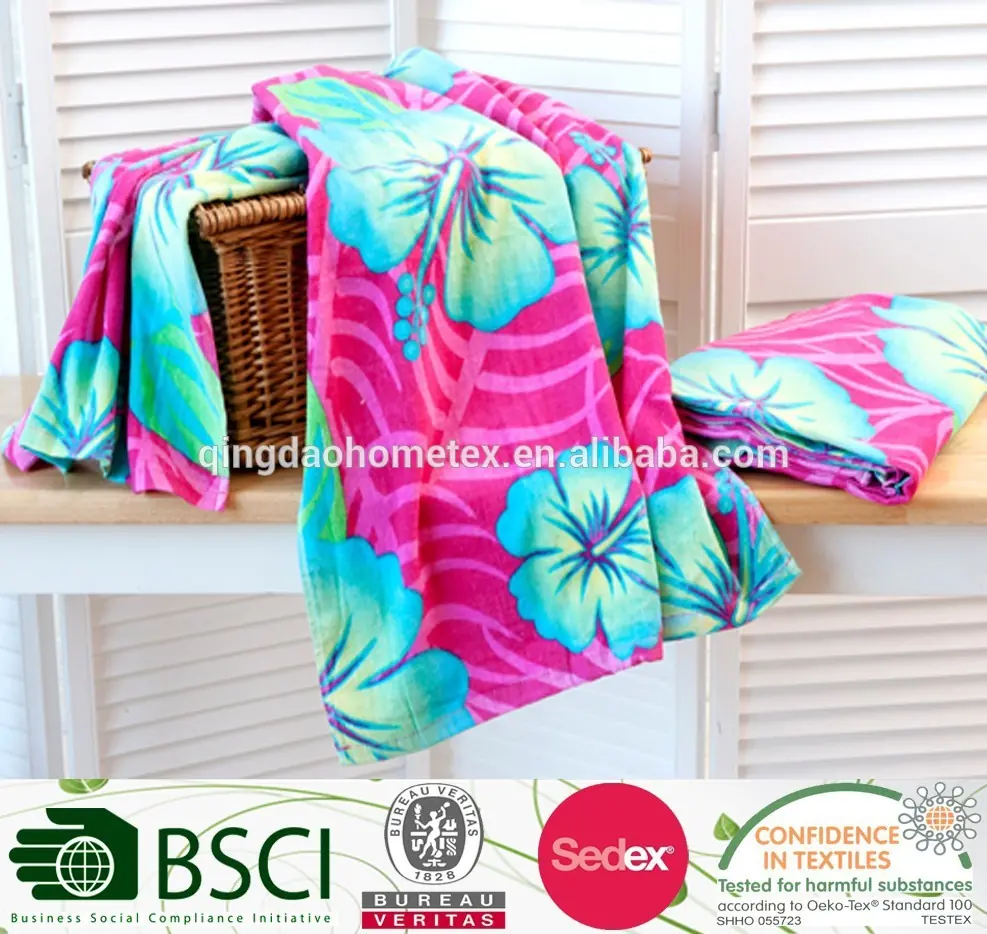 Pink and teal floral-printed beach towels draped over a wicker basket, with a certification banner strip at the bottom.