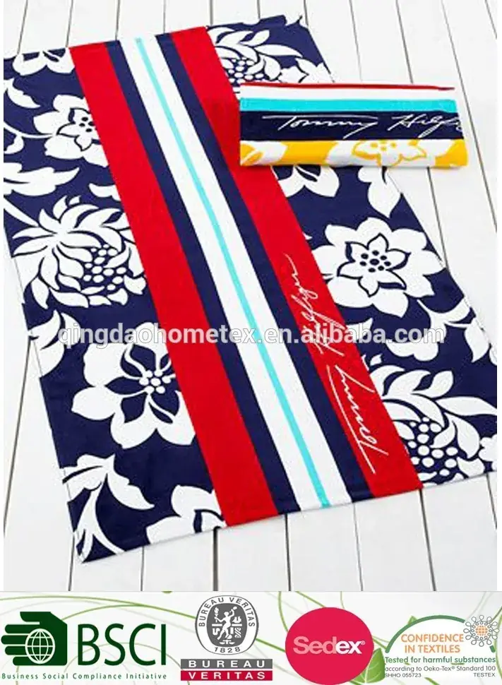 Folded and flat-view beach towels with navy floral print and red, white and blue stripes, with certification logos overlaid at the bottom