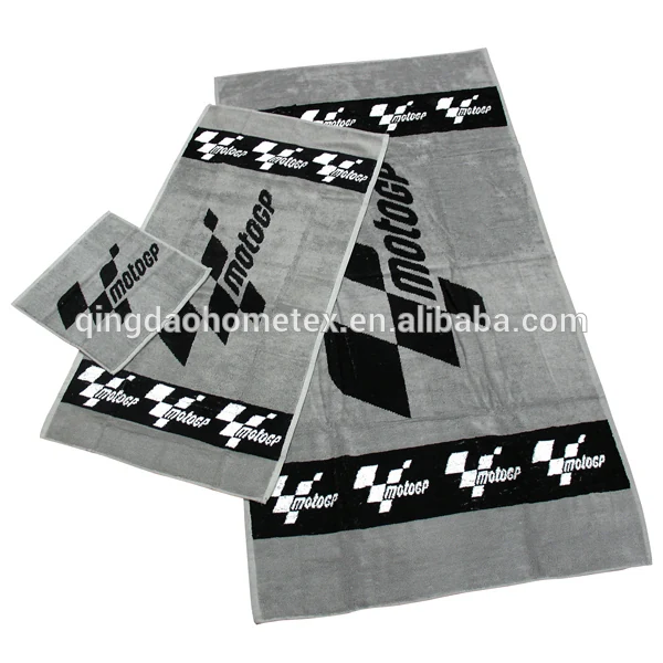 Three grey woven towels in graduated sizes with black checkered MotoGP logo borders, laid flat on white background