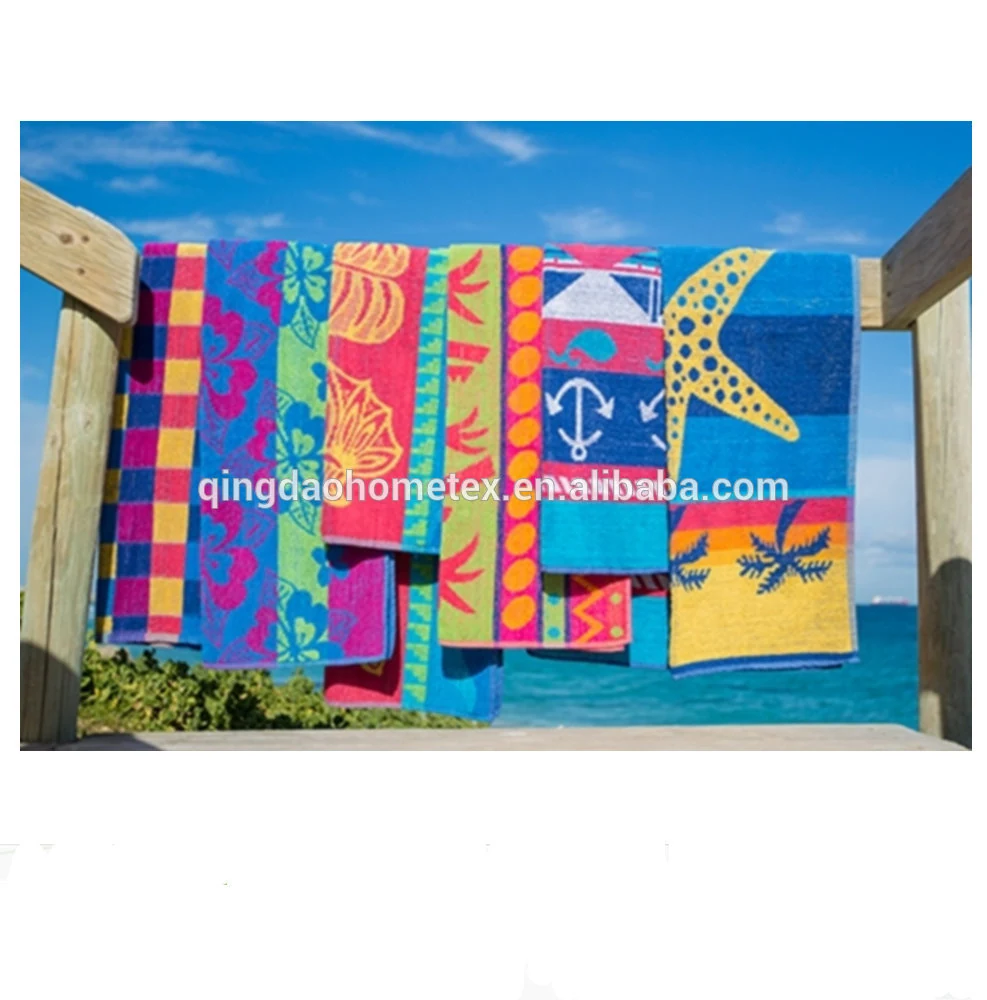 Colorful patterned beach towels with starfish and anchor designs hanging on a wooden rail by the sea