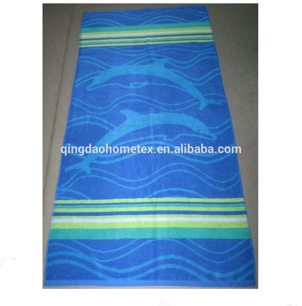 Blue beach towel with dolphin print and green striped borders, laid flat on a gray floor