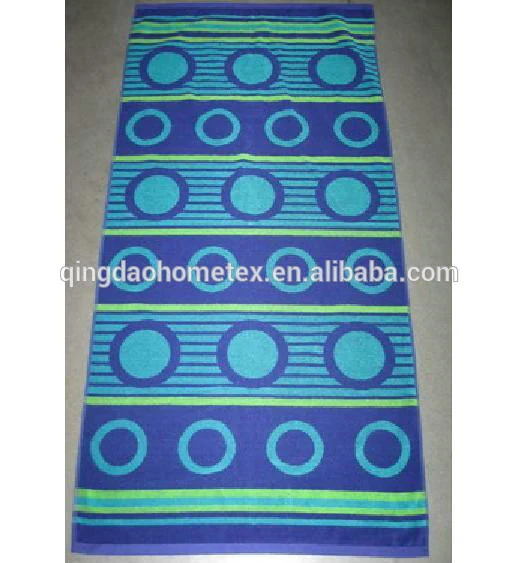 Beach towel with blue and green striped bands and circle patterns, laid flat on a gray floor