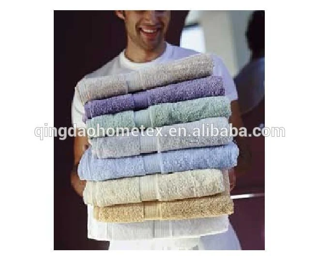Smiling man carrying a tall stack of folded towels in various colors, including beige, purple, blue and cream