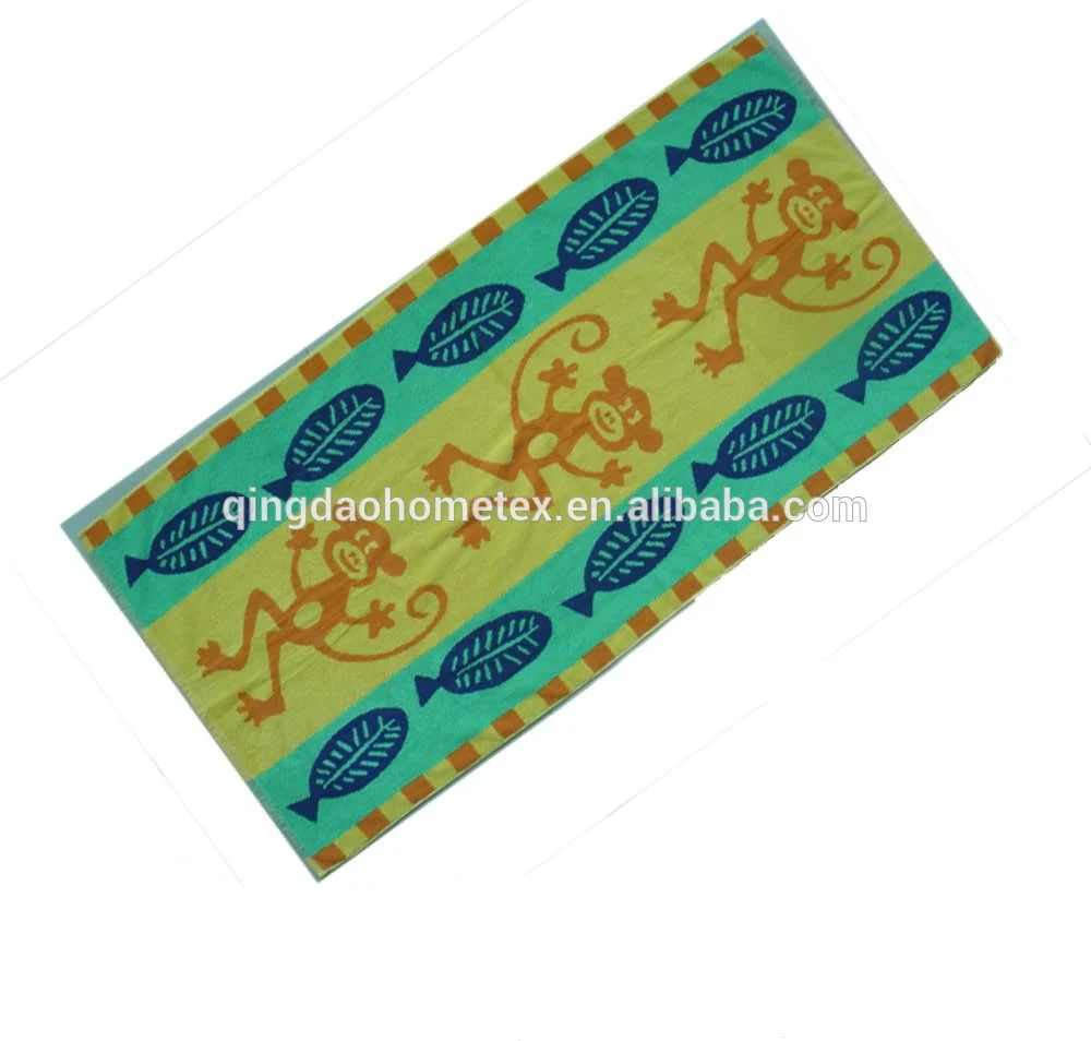 Printed beach towel with orange monkeys and blue fish motifs on green and yellow stripes, shown diagonally
