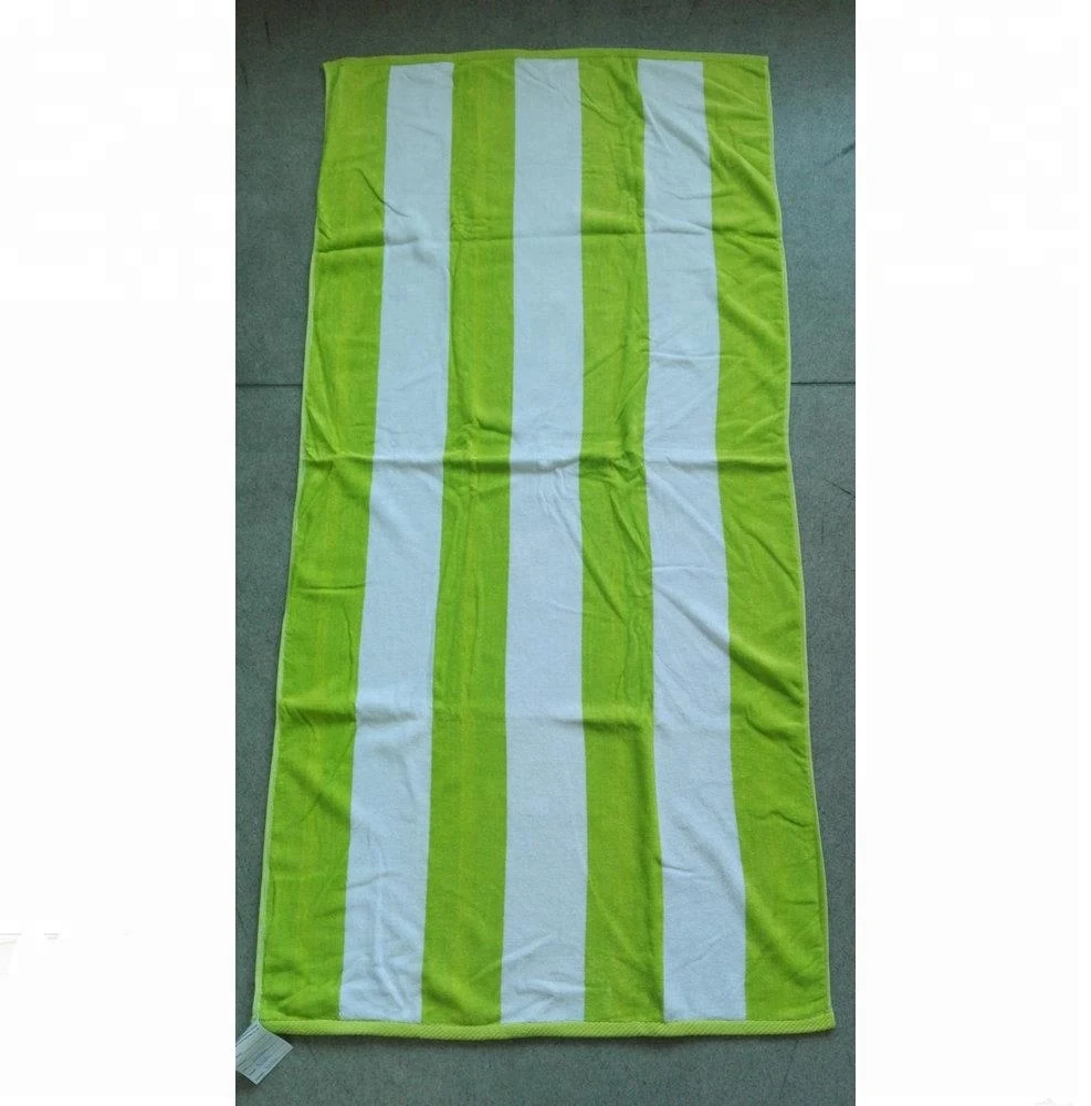 Green and white striped beach towel laid flat on a grey floor