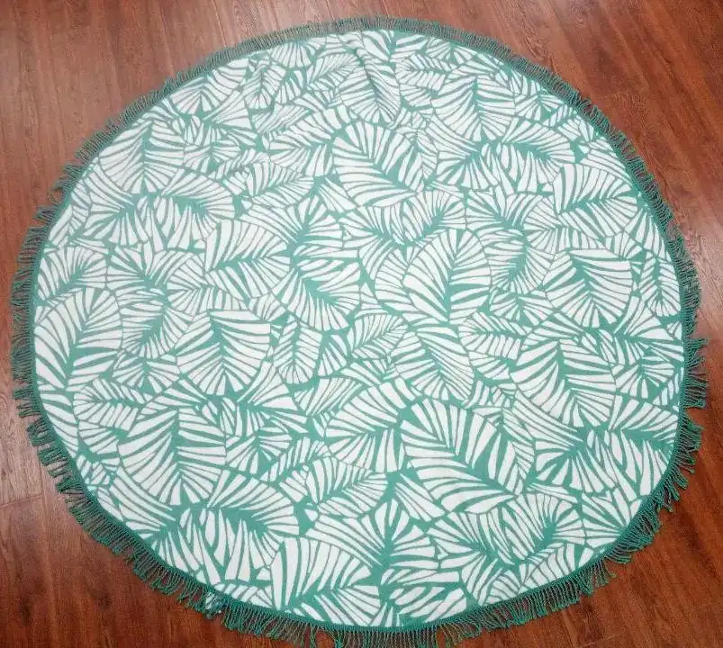 Round green and white leaf-patterned fringe blanket laid flat on a wooden floor