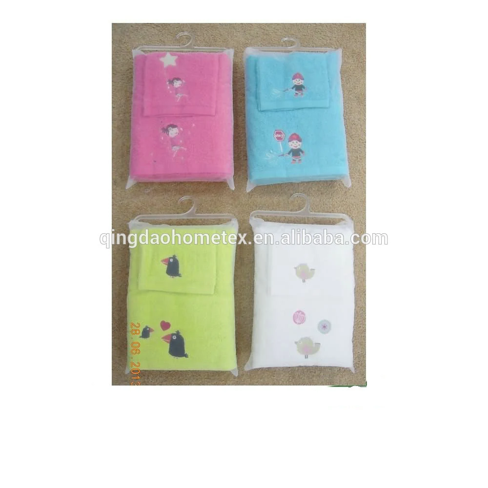 Four packaged children's towel sets in pink, blue, green, and white with cartoon embroidery, hanging on hooks over a carpeted floor