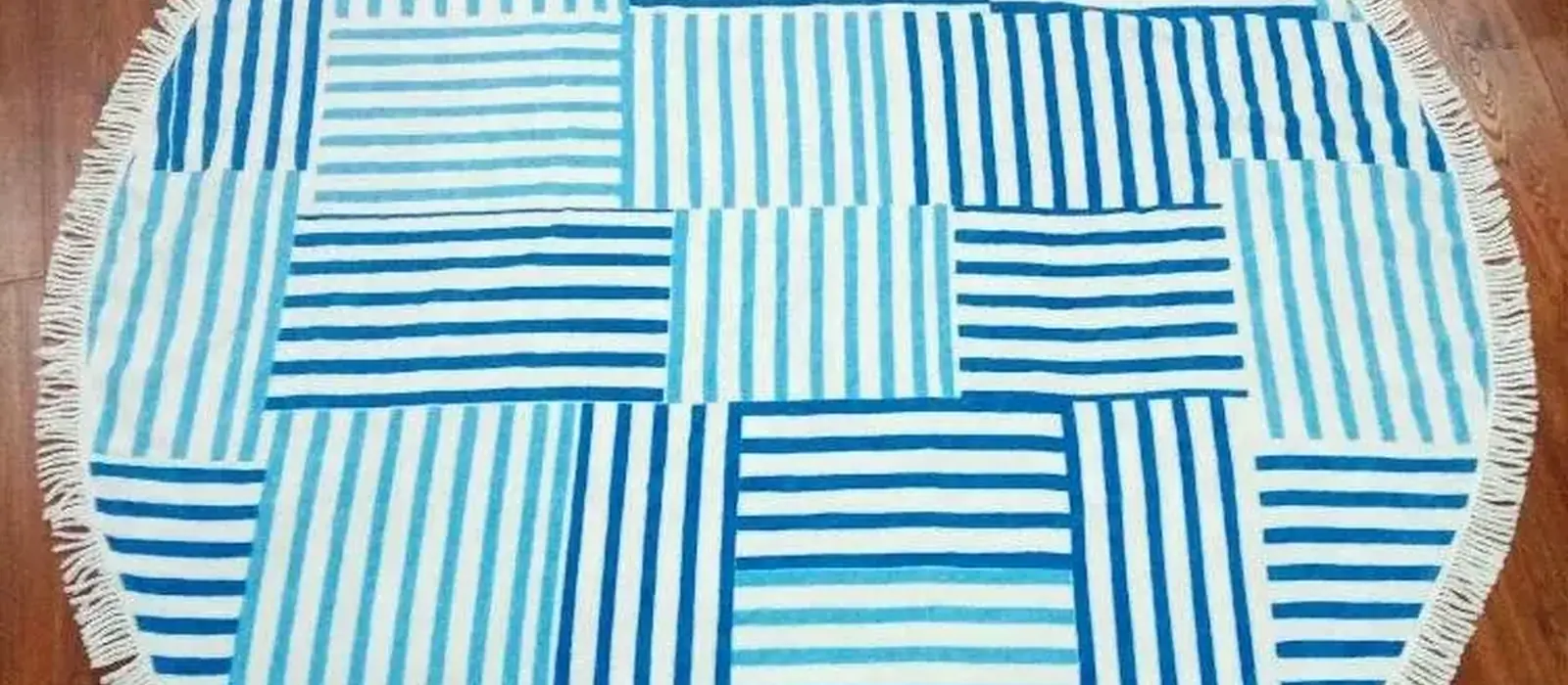 Round beach towel woven in blue and white stripe blocks with a tasselled edge