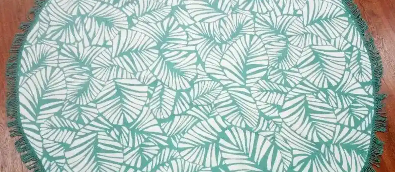 Round cotton beach towel woven with a green leaf pattern and a tasselled edge