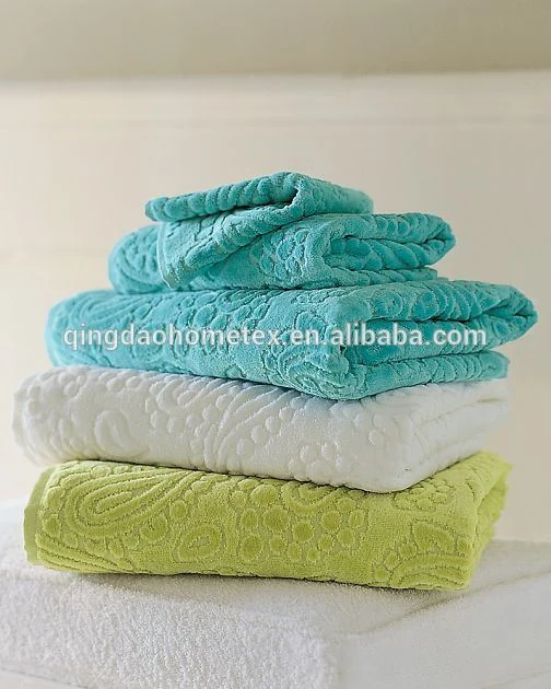 Stack of folded jacquard towels in turquoise, white, and green on a white surface