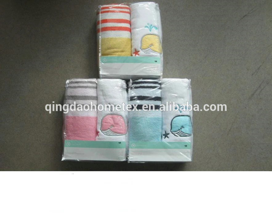 Three packaged kids towel sets with striped and whale-embroidered towels on a grey concrete floor