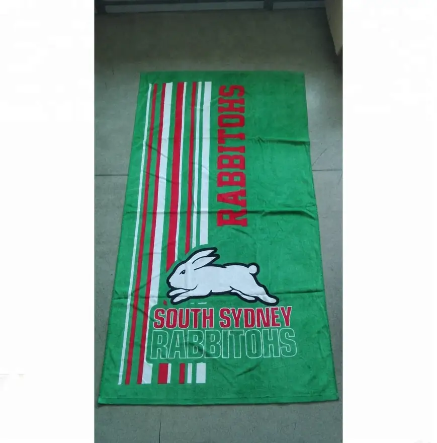 Green beach towel with printed rabbit logo and red and white stripes lying on a tiled floor
