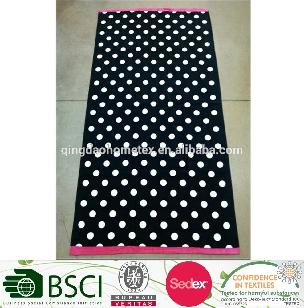 Black beach towel with white polka dots and pink borders laid flat on a tiled floor