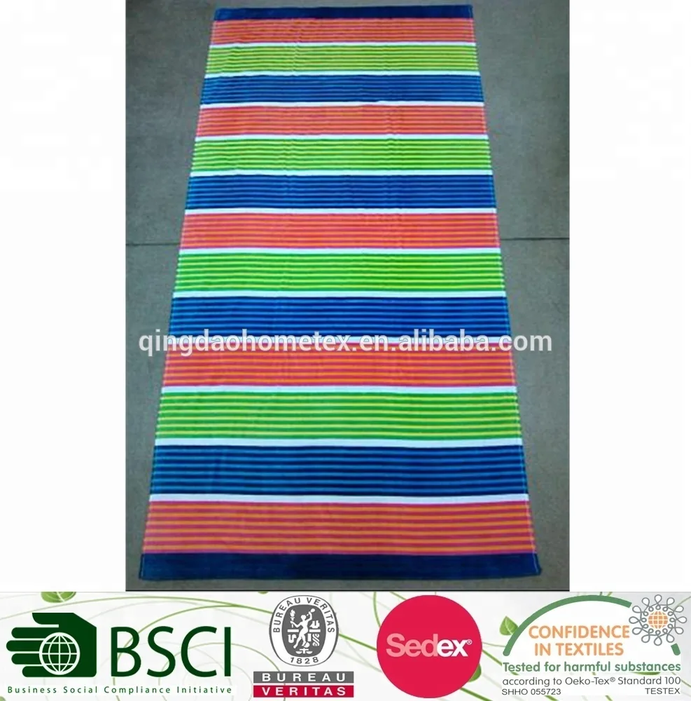 Multicolored striped beach towel in green, blue, coral and orange, laid flat on a gray floor