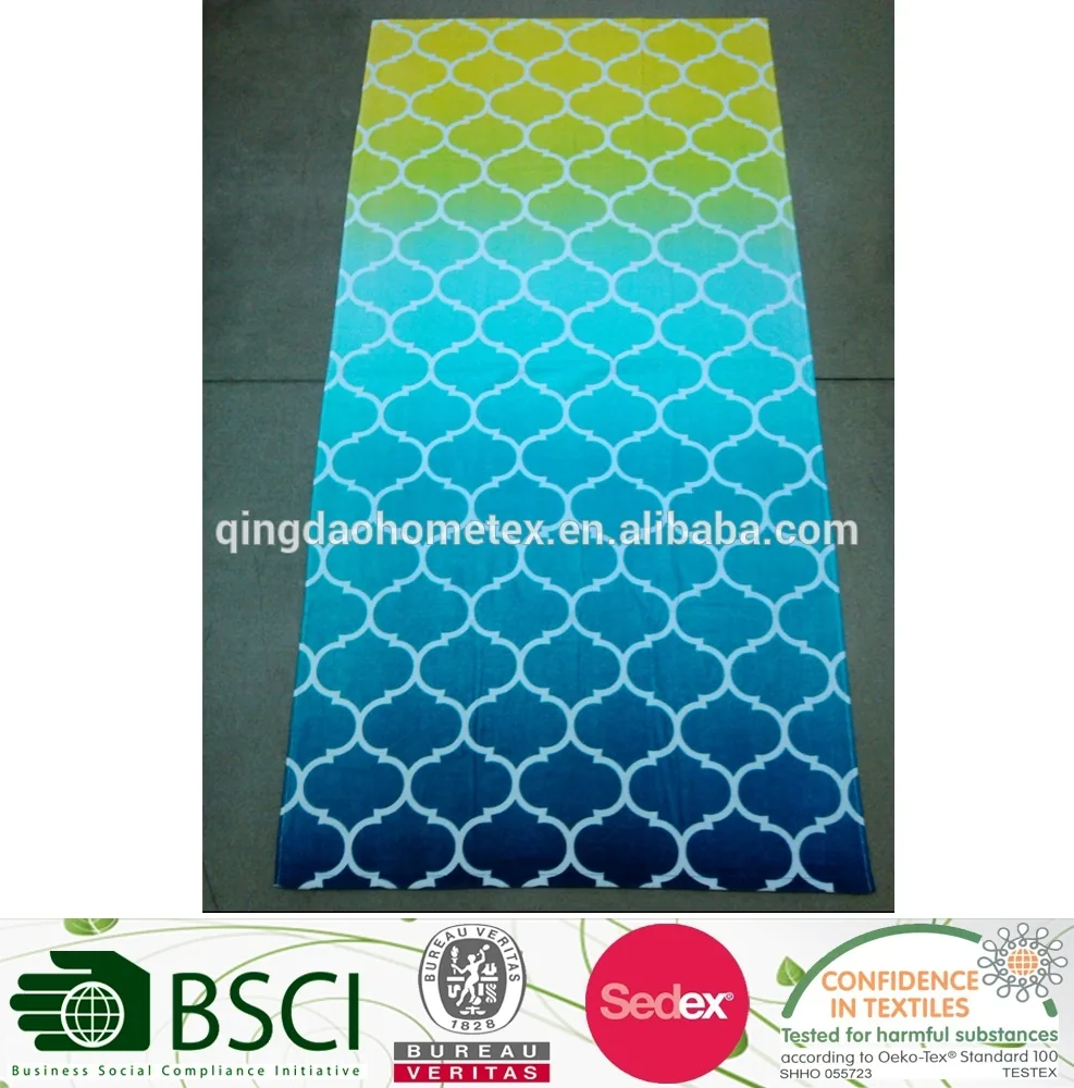 Rectangular printed beach towel with yellow-to-blue gradient and white geometric pattern, lying on a concrete floor