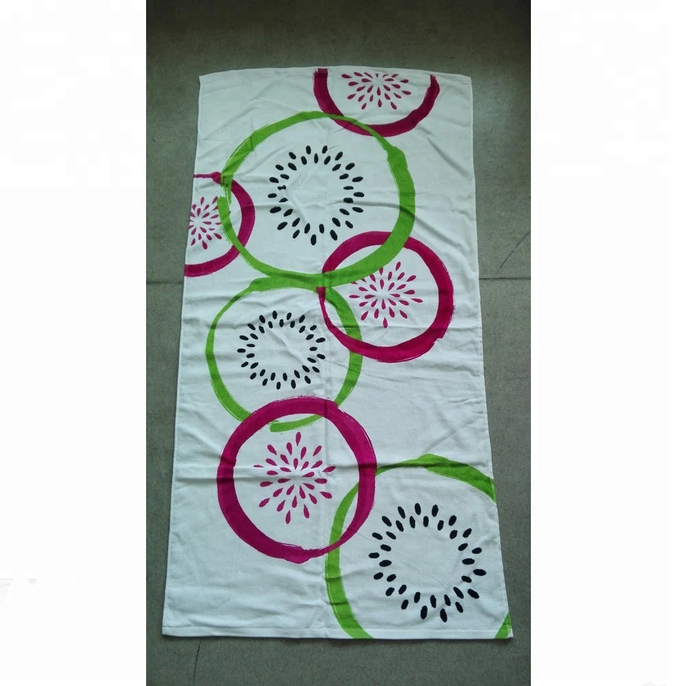 White beach towel printed with pink and green circular patterns and black burst motifs, laid on a tile floor