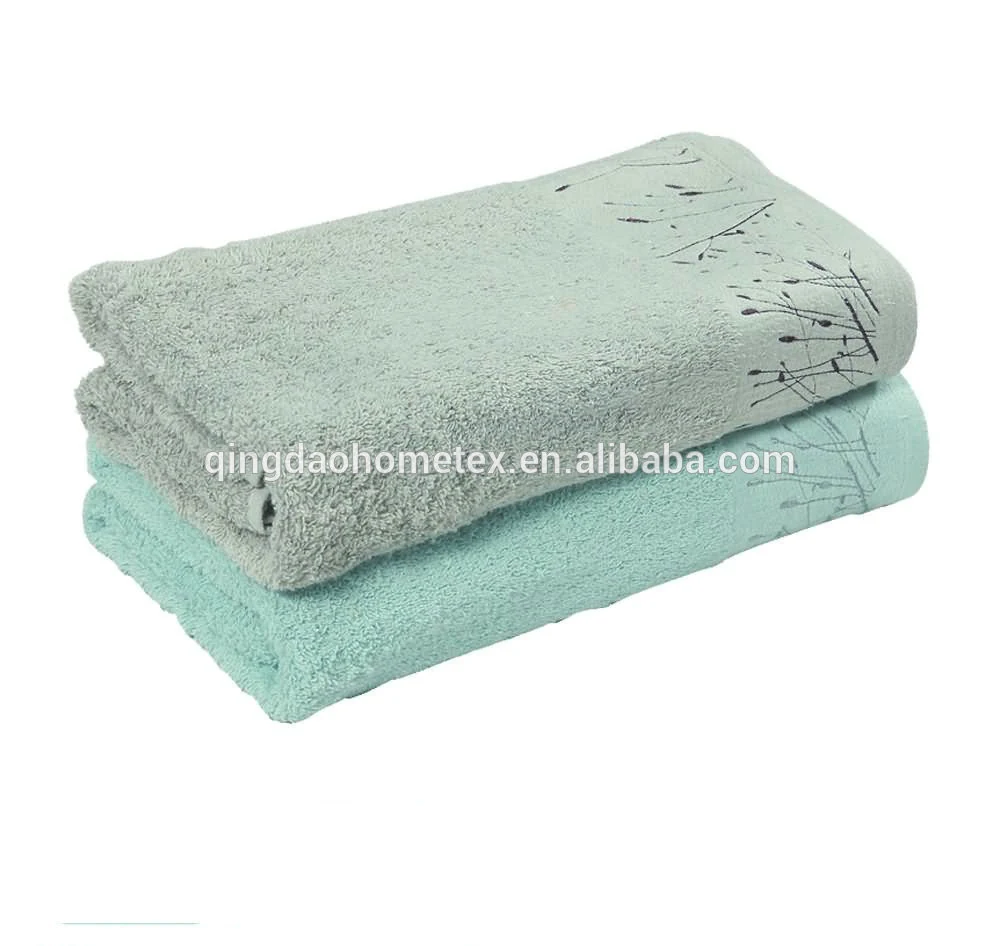 Two folded towels in grey-green and mint tones with a dark botanical print, stacked on a white background.