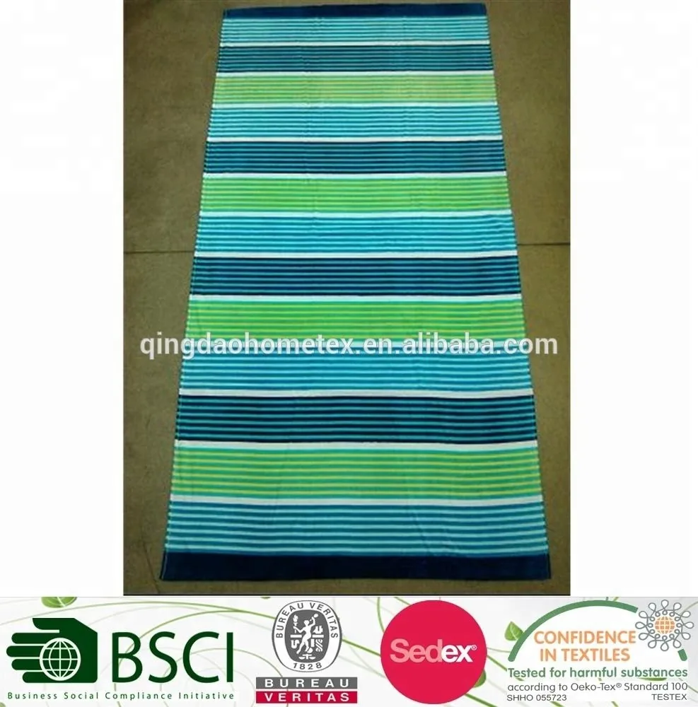 Striped beach towel in green, blue, teal, and white laid flat on a concrete floor