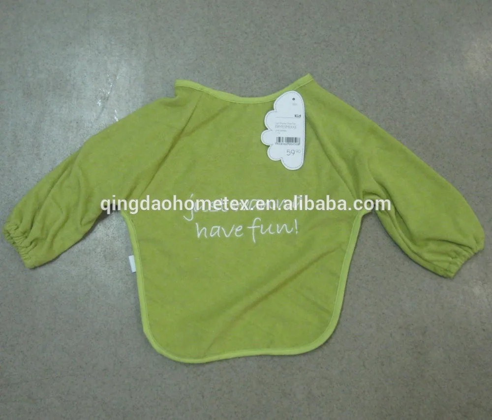 Green long-sleeve baby bib with embroidered text and a paper tag, laid flat on a gray floor