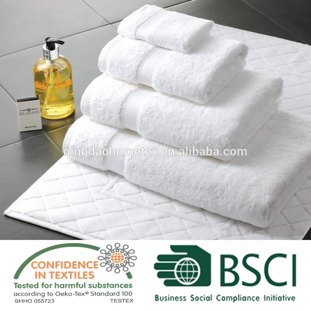 Stack of folded white hotel towels on a tiled surface with a bath mat and toiletry bottles, certification logos overlaid at bottom.