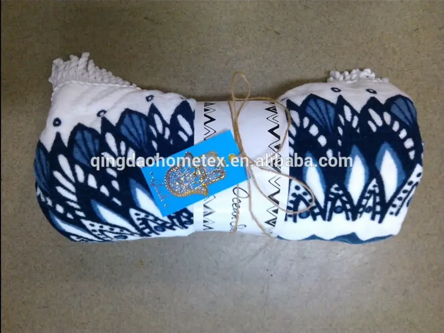 Rolled white blanket with navy blue ikat-style print, fringe ends, tied with string and a blue tag