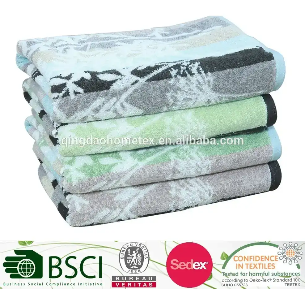 Stack of folded yarn-dyed towels with floral leaf patterns in grey, black, blue and green on a white background.