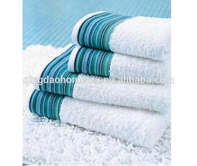 Stack of folded white terry towels with blue and teal striped borders on a light background