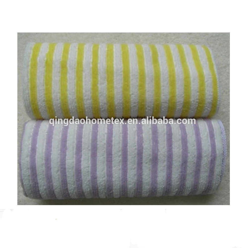 Two rolled striped terry towels, one yellow and white and one purple and white, on a textured surface