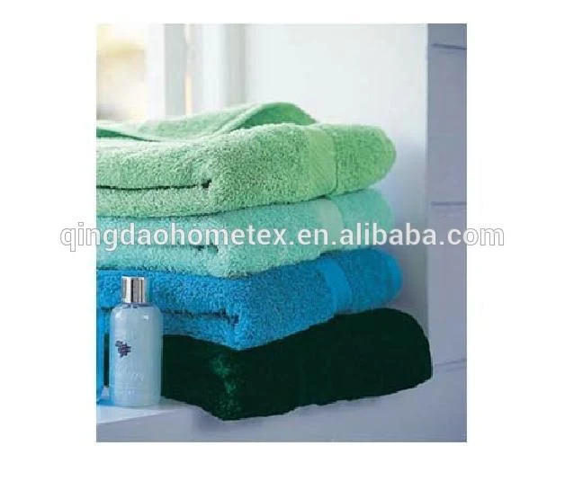 Stack of folded towels in green, teal, blue, and dark green beside a small bottle on a white windowsill