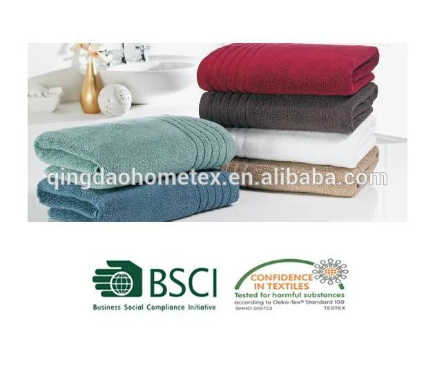 Stacks of folded towels in blue, teal, gray, red, white, and tan on a white bathroom counter with a sink and vase