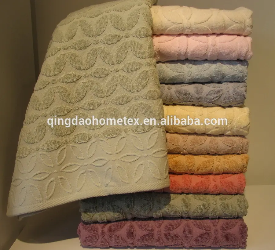 Stack of folded cotton towels in assorted pastel colors with floral jacquard weave, one towel draped in front
