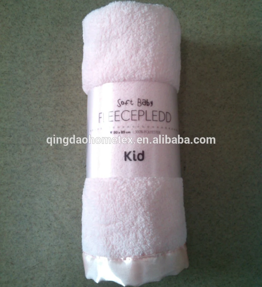 Rolled pale pink fleece baby blanket with satin trim and printed packaging band reading Kid