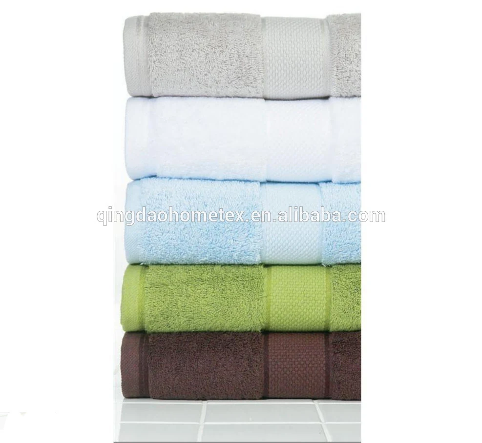 Stack of folded terry towels in grey, white, light blue, green, and brown on a white tiled surface