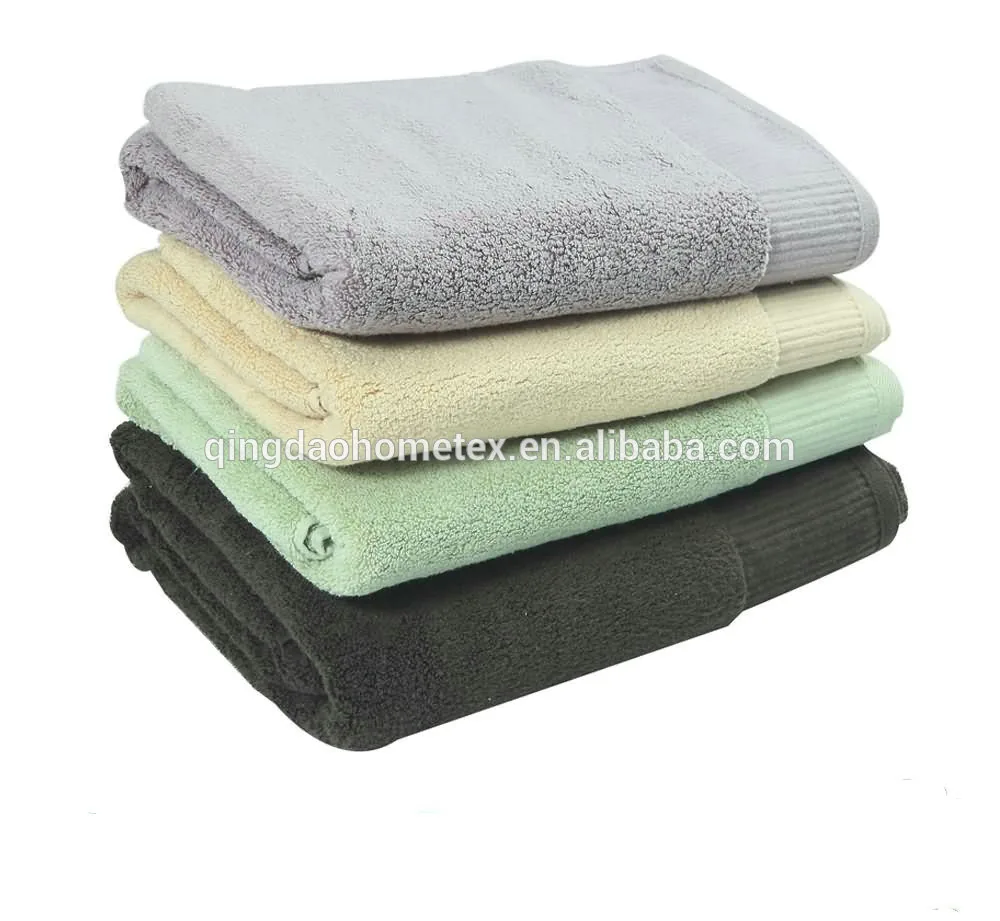 Stack of four folded terry towels in grey, cream, green and dark charcoal on a white background