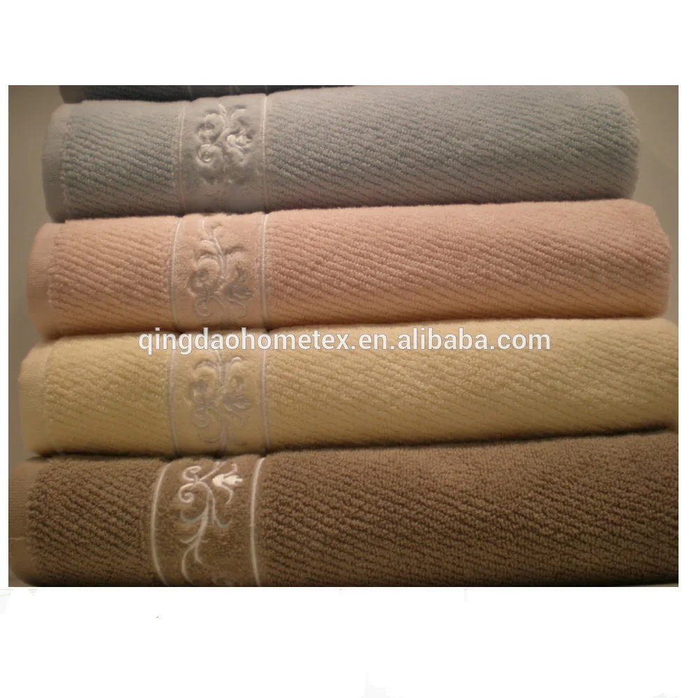 Stack of four folded terry towels in grey, pink, cream, and brown with embroidered floral bands