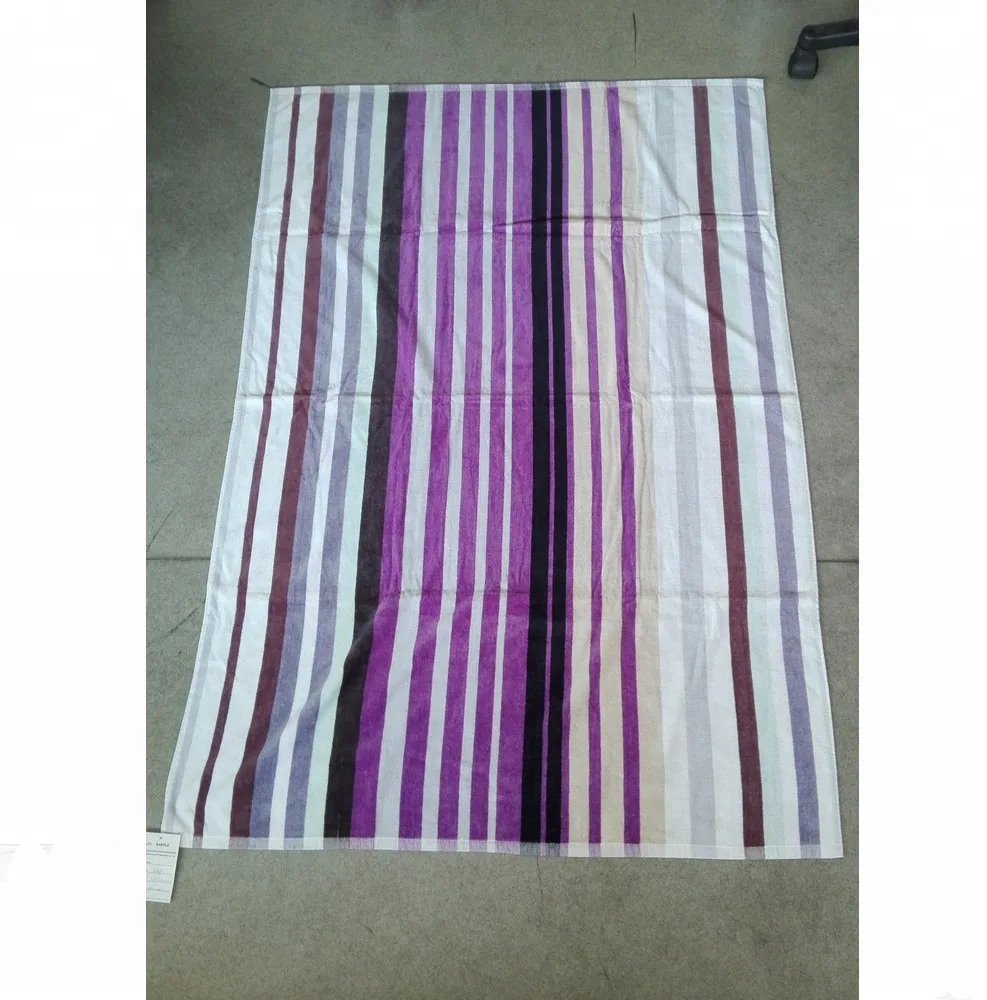 Striped towel or fabric with purple, magenta, black and white vertical stripes laid flat on a gray floor