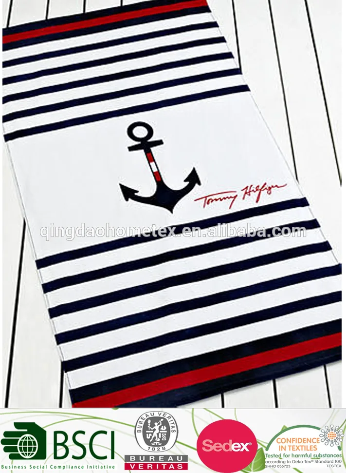 Navy, white and red striped beach towel with black anchor print and red script lettering, shown flat on a white slatted surface
