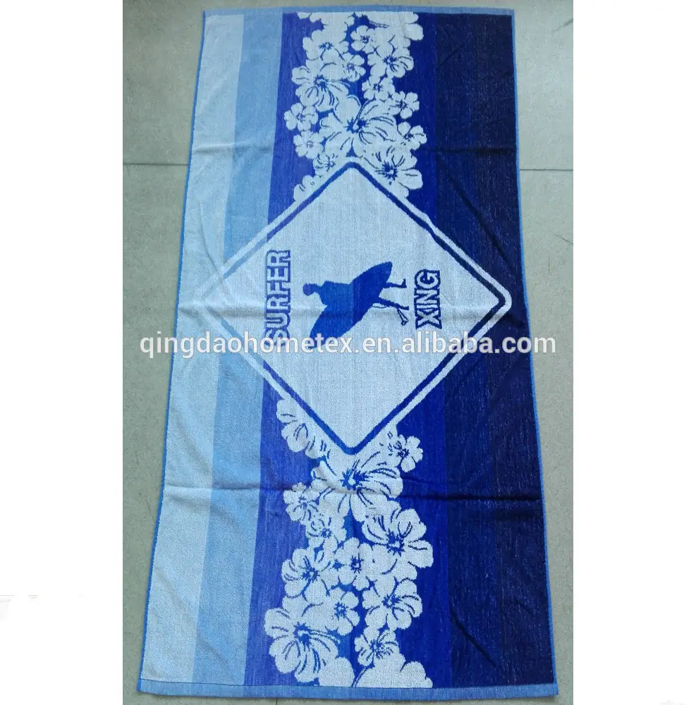 Blue and white floral beach towel with a surfer graphic and 'SURFER' text, photographed flat on a tiled floor