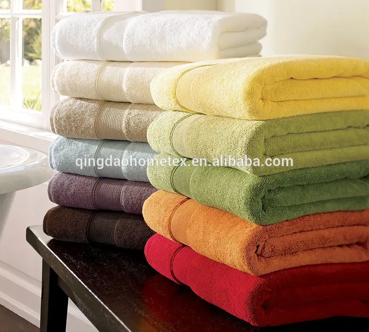 Stacks of folded bath towels in assorted colors on a dark table beside a bright window