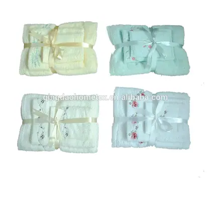 Four folded embroidered towel gift sets in cream, mint and white, each tied with a satin ribbon bow
