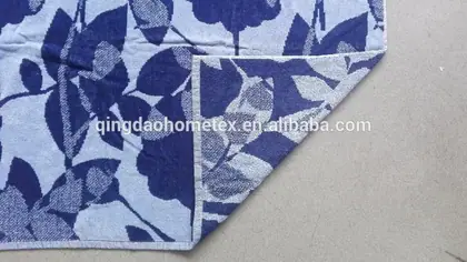 Light blue towel or blanket with dark blue floral leaf pattern, folded corner showing reverse side on gray floor