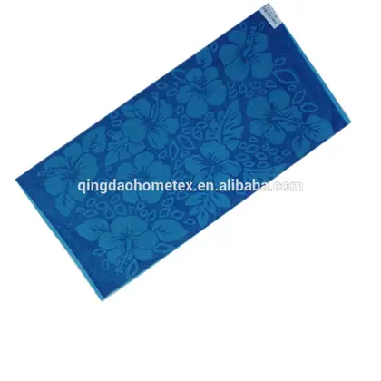Blue jacquard beach towel with hibiscus flower pattern and small fabric tag, laid diagonally on white background