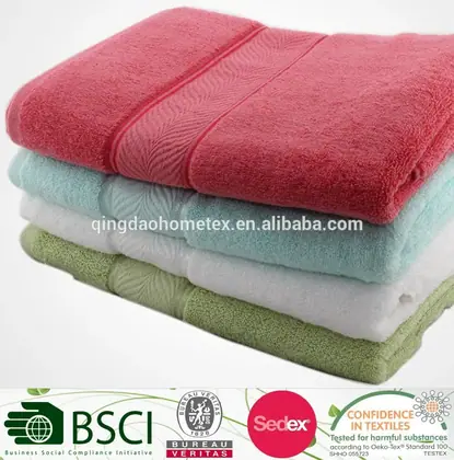 Stack of folded coral, teal, white and sage green cotton towels on a plain light background