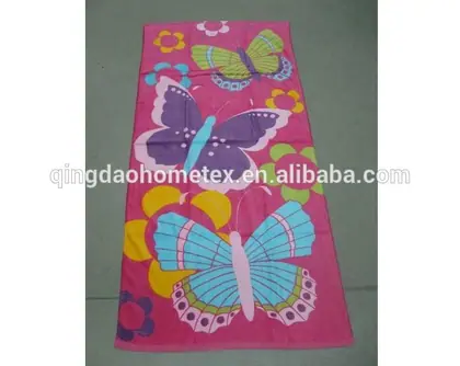 Pink beach towel printed with colorful butterflies and flowers, laid flat on a gray floor