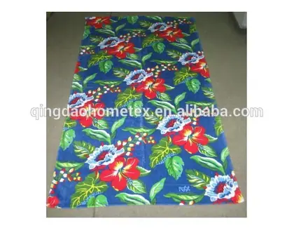 Blue beach towel with red hibiscus flowers and green leaves laid flat on a floor