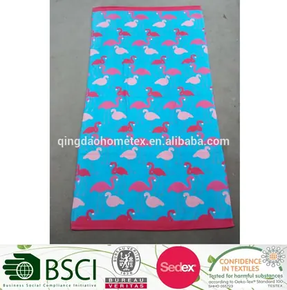 Turquoise beach towel with pink and white flamingo print laid flat on a concrete floor